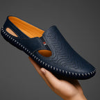 Navy perforated leather slip-on held in a hand, showing the side cutouts and whipstitched edge from above