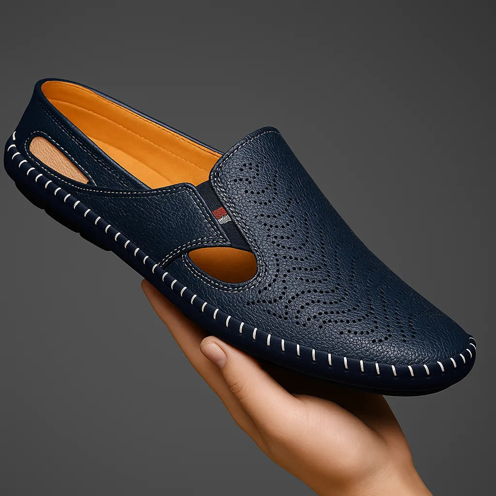 Navy perforated leather slip-on held in a hand, showing the side cutouts and whipstitched edge from above
