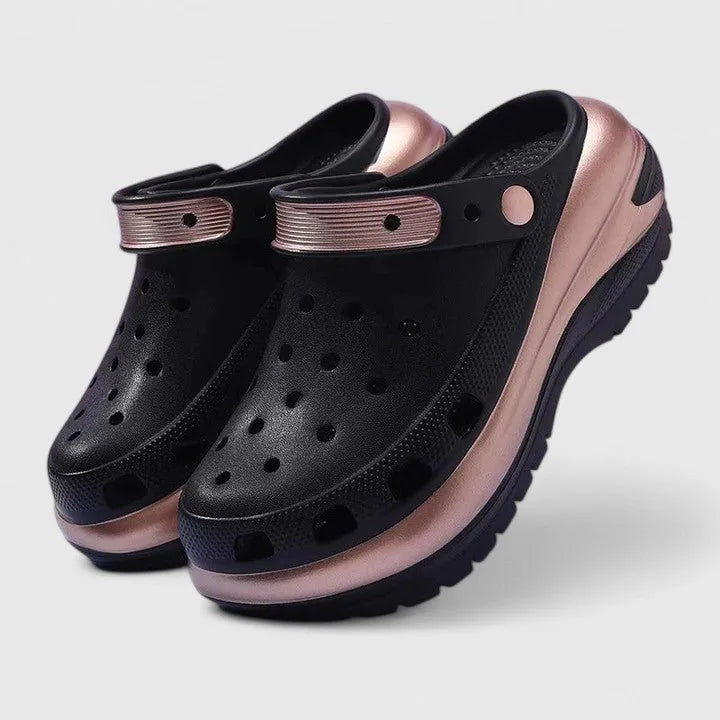 Pair of black clogs with perforated upper, rose gold heel strap and thick chunky platform sole, shown at angle
