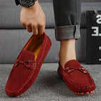 Hand holding a wine red perforated suede loafer with mustard interior lining, paired with matching shoe worn on foot