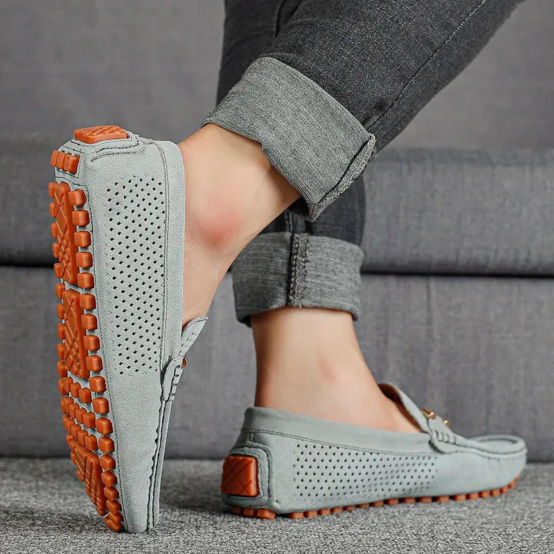 Sole view of a grey suede driving loafer worn on foot, showing textured orange rubber pebble outsole in full