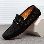 Black suede perforated loafer with bow lace and orange rubber sole, photographed on a light grey background