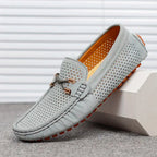 Grey suede perforated loafer with bow lace and orange rubber sole, angled side profile on textured flooring