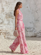 Side profile of the flowing wide-leg jumpsuit, showing the fluid drape of the fabric while walking on sand