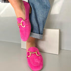Side view of hot pink suede loafer with gold horsebit buckle, worn on foot with cuffed blue jeans against a white wall.