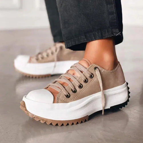 Side view of beige and brown platform sneaker with white toe cap and chunky tread sole, worn with black trousers
