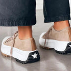 Back view of two beige suede platform sneakers showing star-studded chunky soles and black trousers rolled above the ankle