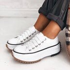 White lace-up platform sneaker with silver eyelets shown next to a black leather jacket and cuffed black trousers
