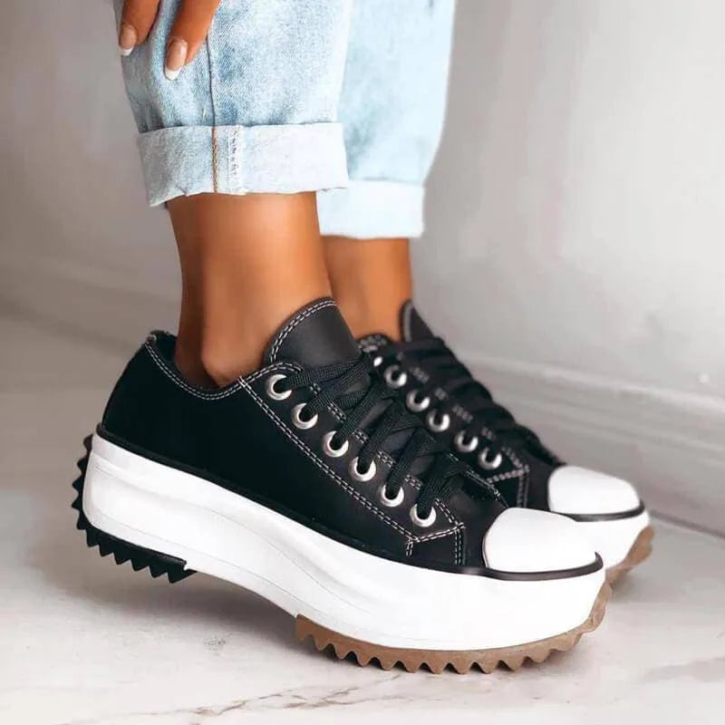 Black and white platform sneaker with silver eyelets and gum sole shown resting beside a hand with painted nails