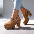 Tan platform clogs with crossover buckle straps shown mid-stride against a plain studio backdrop