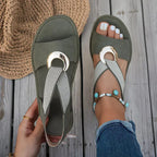 Top view of a green sandal with crossover woven straps and gold ring hardware, held in hand against a wooden deck