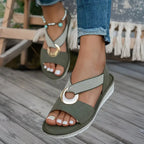 Model wearing green crossover strap sandals with gold hardware, styled with cuffed denim jeans outdoors