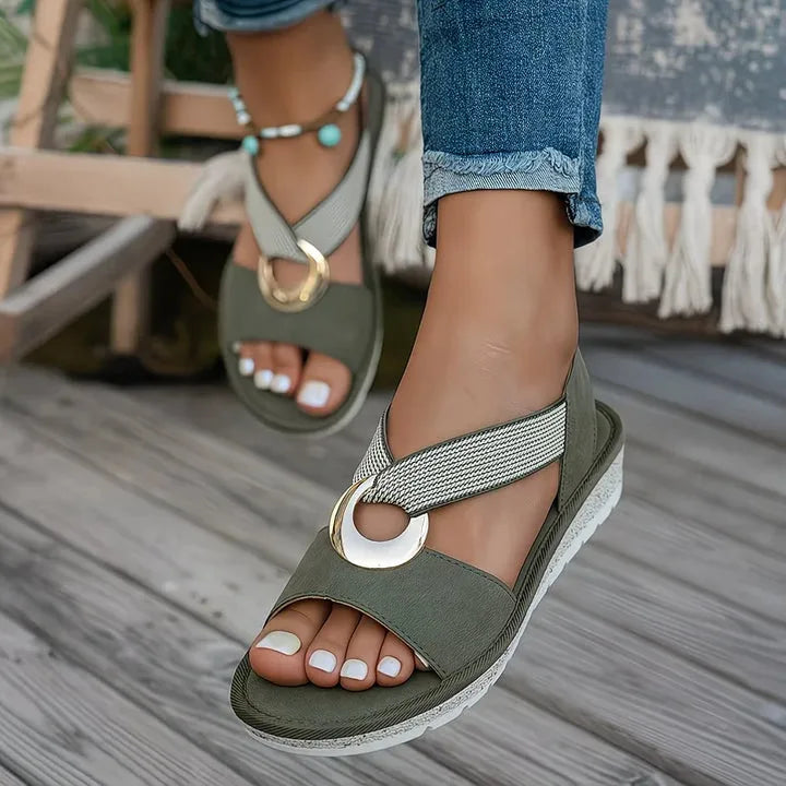 Model wearing green crossover strap sandals with gold hardware, styled with cuffed denim jeans outdoors