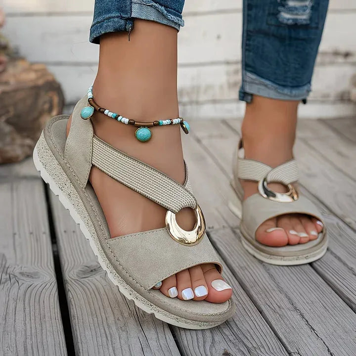 Close-up of beige sandals on foot showing padded platform sole, turquoise beaded anklet and crisscross straps