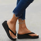 Profile shot of a woman stepping in black platform flip-flops, highlighting the thick 7cm wedge sole and smooth rubber finish