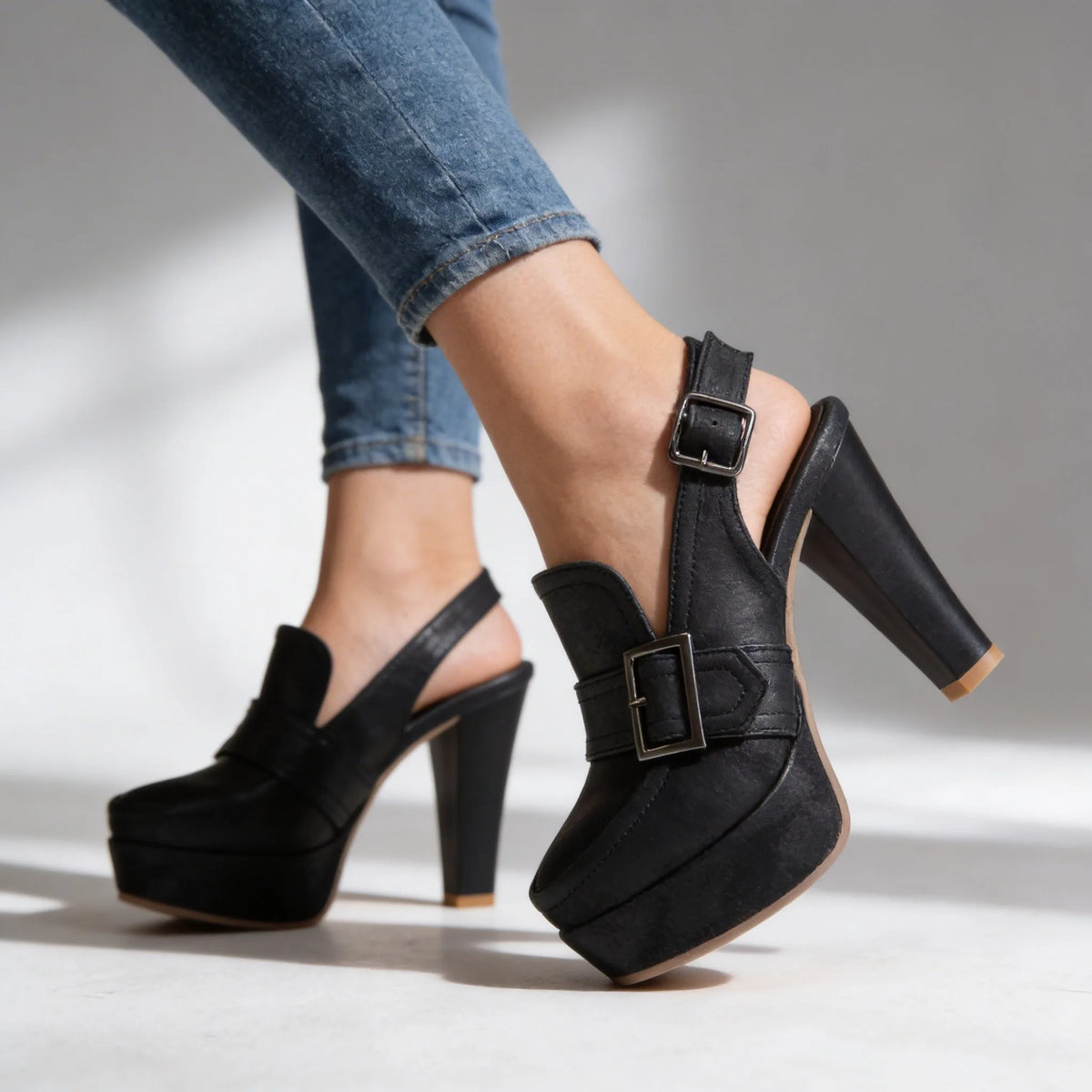 Studio shot of black platform slingback heels on crossed legs against a plain backdrop, showing buckle and heel height