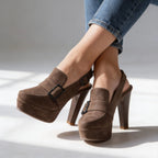 Detailed studio view of khaki suede-textured platform heels with dark buckle hardware and stacked block heel