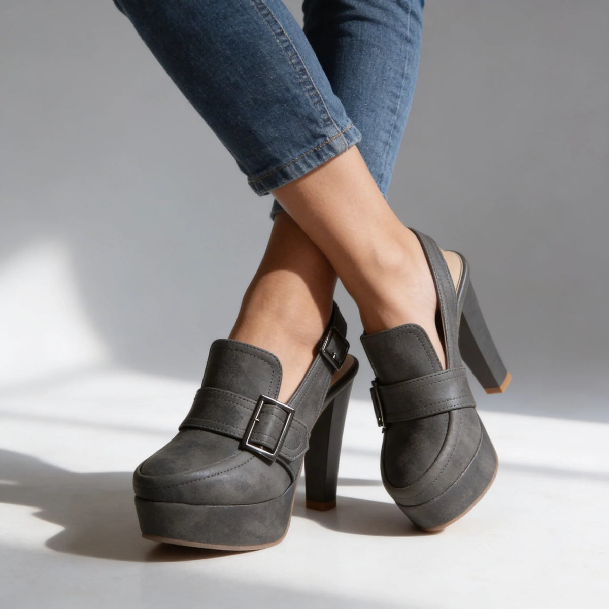 Studio image of grey platform slingback heels on crossed ankles, showing the sling strap and block heel from the side