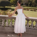 Woman on a stone balustrade wearing a white strapless corset-style midi dress with a pleated full skirt
