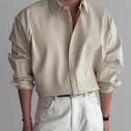 Close-up front view of a man wearing a cream pleated textured long-sleeve shirt with a white belt and white trousers