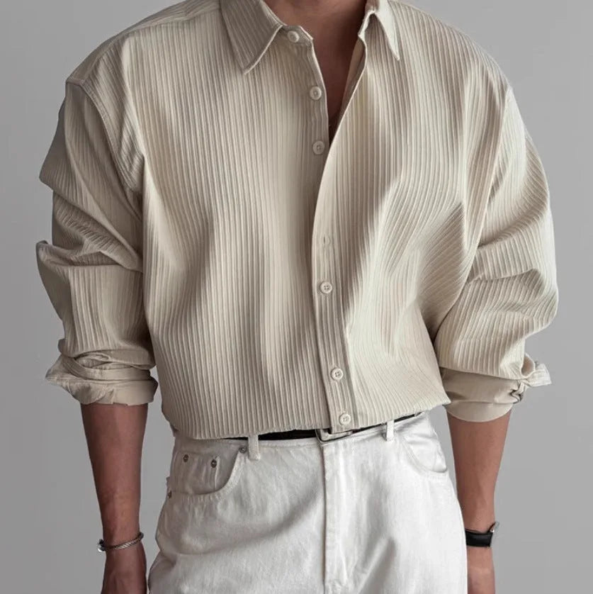 Close-up front view of a man wearing a cream pleated textured long-sleeve shirt with a white belt and white trousers