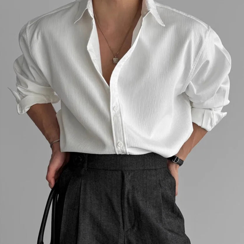 Front view of a white pleated textured shirt worn open at the collar with charcoal pleated trousers