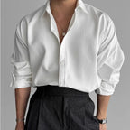 Close-up of a white pleated textured shirt with a classic collar worn over dark grey tailored trousers