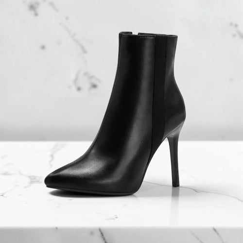Side profile of a black leather ankle boot with pointed toe and thin stiletto heel on a marble surface