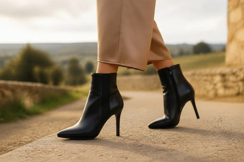 Woman walking outdoors wearing black pointed-toe stiletto ankle boots with camel wide-leg trousers