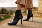 Back angle of black stiletto ankle boots highlighting the seam detail and heel shape while walking