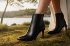 Close-up of black leather ankle boots on grass, paired with a flowing light-colored skirt near a lake