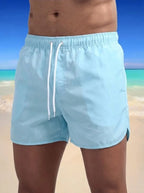 Close-up front view of pale blue boardshorts with white drawstring and elastic waistband, worn on the beach