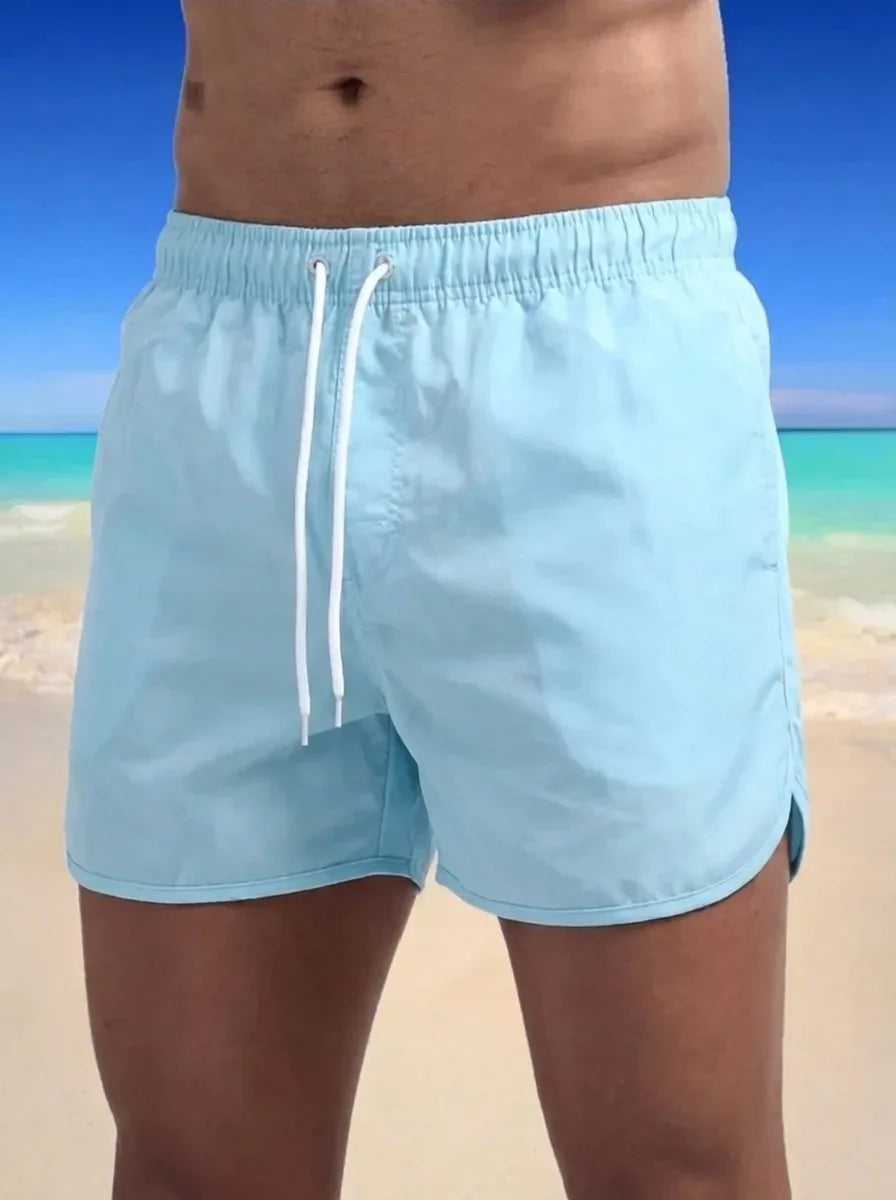 Close-up front view of pale blue boardshorts with white drawstring and elastic waistband, worn on the beach