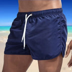 Side view of navy blue boardshorts showing the metal eyelets and elastic waist on a sandy backdrop