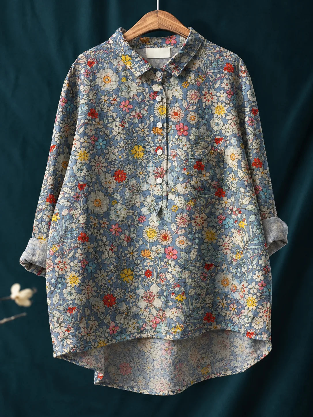 Blue ground shirt covered in a dense ditsy floral print of white daisies, pink and yellow flowers