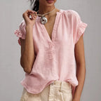 Close-up of pink linen-look blouse with V-neckline, button placket and ruffled cap sleeve, worn with a knot pendant necklace