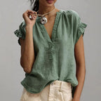Green V-neck blouse with button placket and soft ruffle cap sleeves, paired with cream trousers