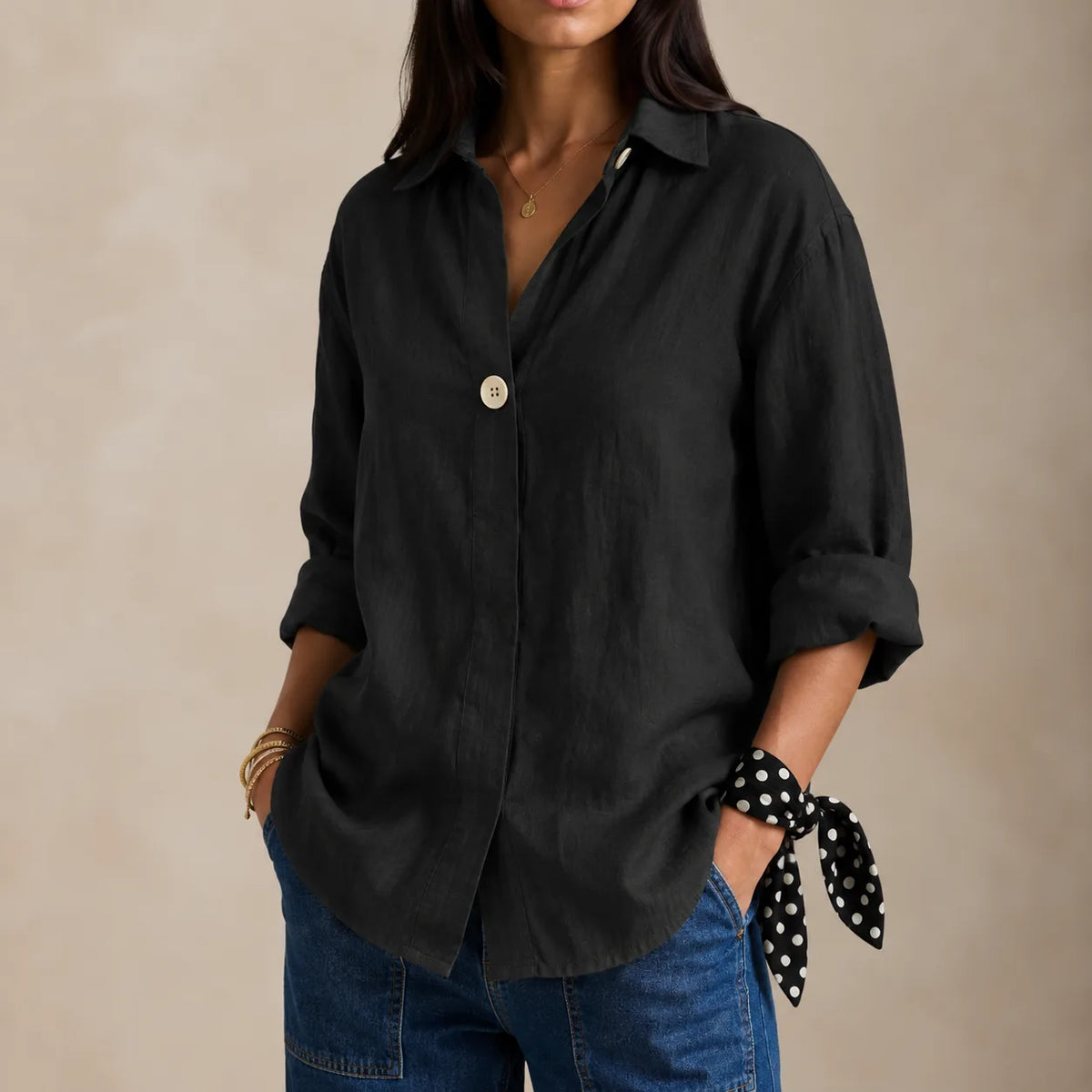 Black linen blouse with relaxed V-neckline, rolled three-quarter sleeves and curved hem over jeans