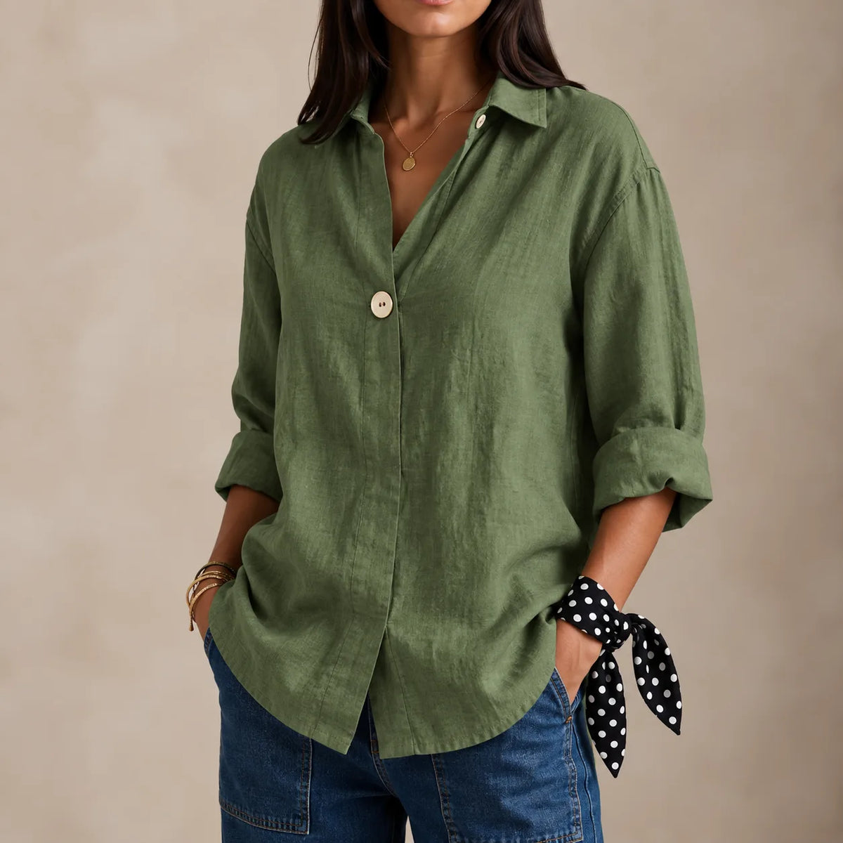 Green linen blouse with single button closure and relaxed fit, worn with layered gold bracelets