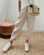 Beige linen relaxed pants with drawstring waist, cuffed hems and white sneakers, close front view
