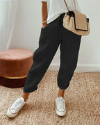 Black linen relaxed pants with drawstring waist and rolled cuffs, styled with white sneakers