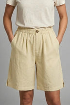 Close-up front view of beige linen shorts with button waist detail and side slit at hem