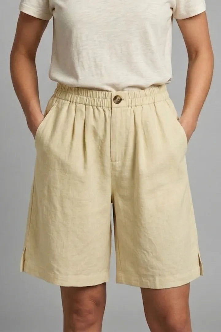 Close-up front view of beige linen shorts with button waist detail and side slit at hem