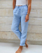 Front view of light blue linen pants with drawstring waist, side pockets and rolled cuffs, worn with bare feet