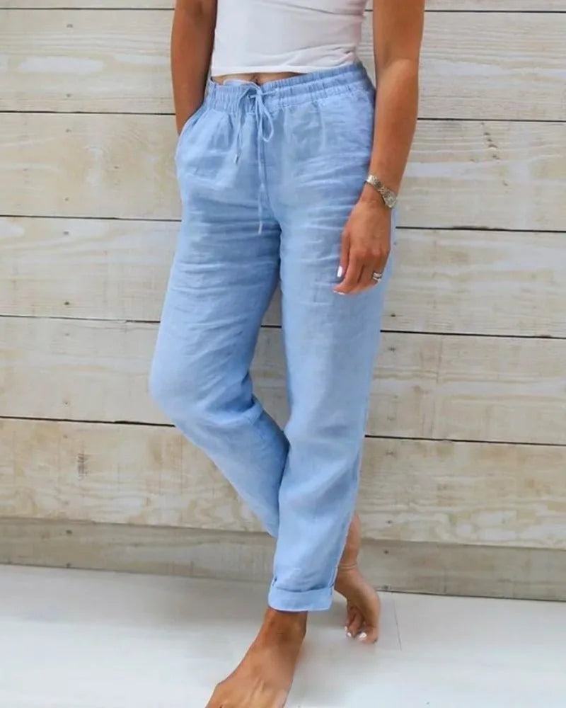 Front view of light blue linen pants with drawstring waist, side pockets and rolled cuffs, worn with bare feet
