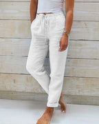 White linen trousers with drawstring tie waist, side pockets and straight leg, worn barefoot