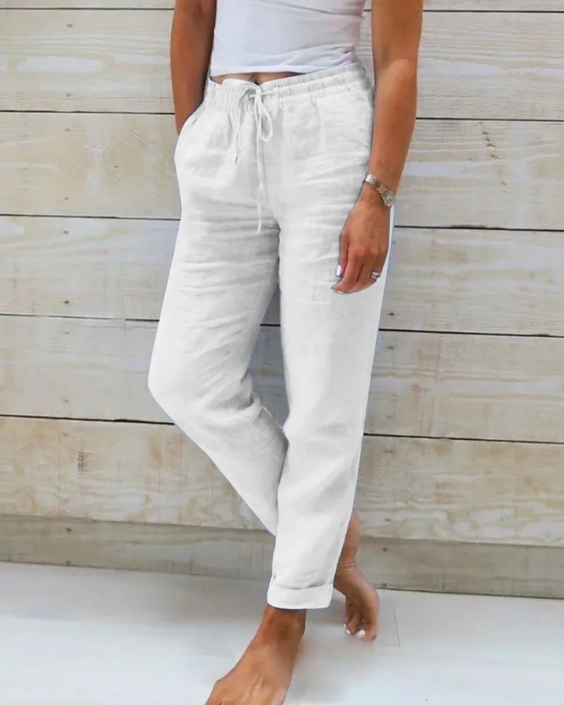 White linen trousers with drawstring tie waist, side pockets and straight leg, worn barefoot
