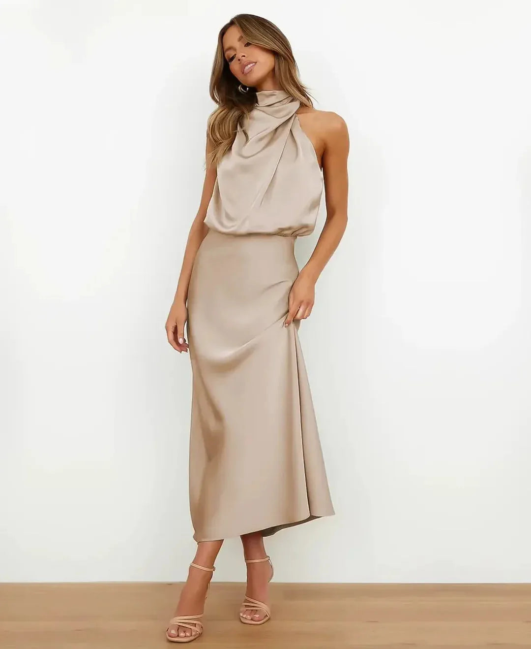 Front view of model in champagne satin midi dress with draped cowl neckline and halter straps