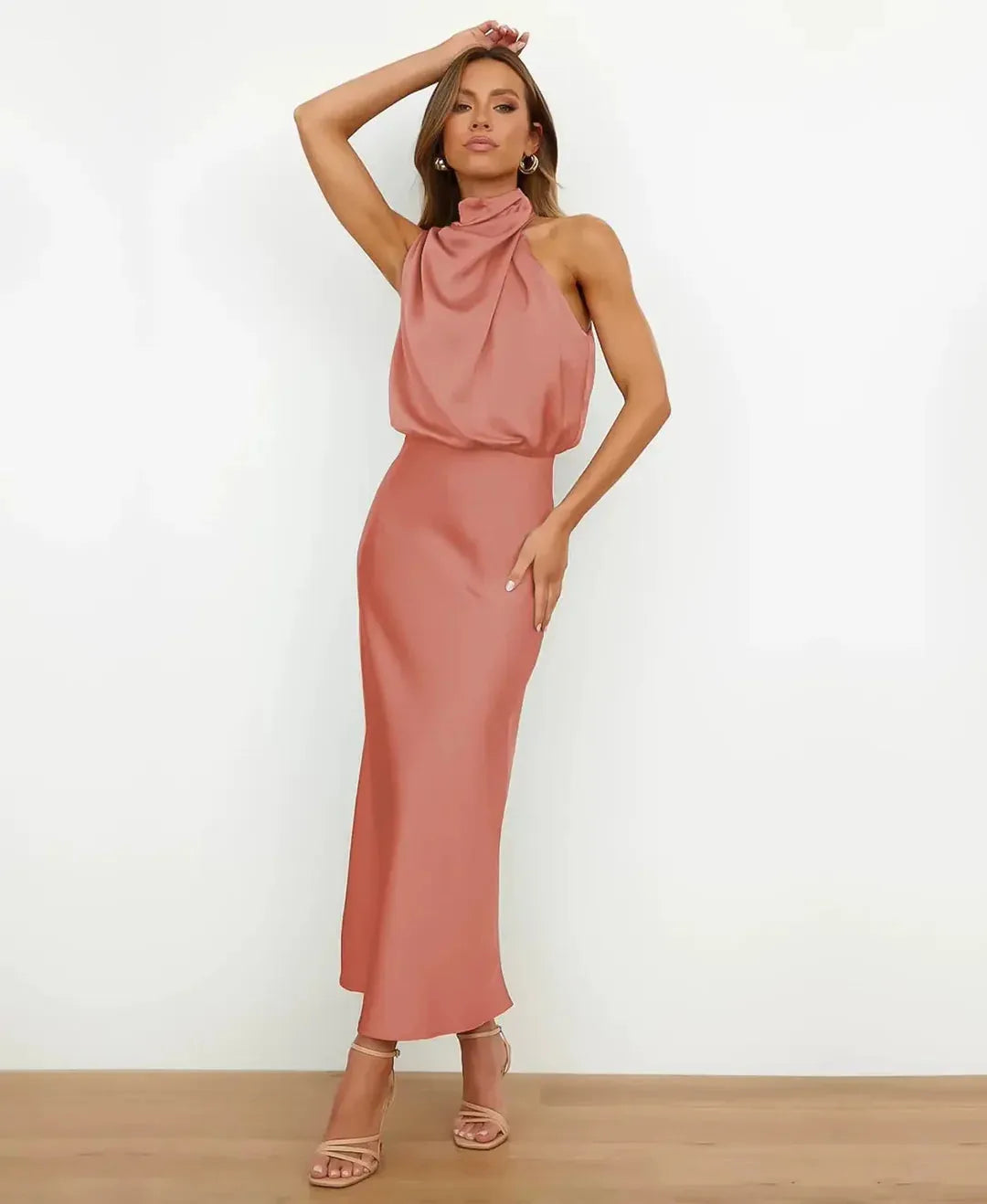 Front view of model in peach satin halter dress, hand raised, showing draped bodice
