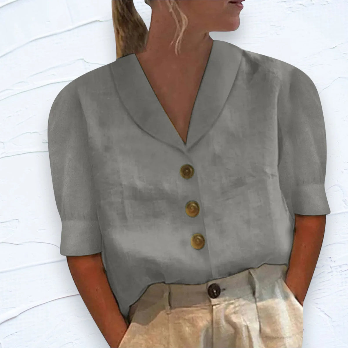 Grey shawl V-neck top with cap sleeves and button placket, shown against a white textured wall backdrop